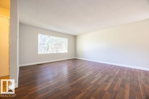 Spacious room with dark wood-finish flooring, light grey walls, white baseboards, and a large window - 8714 164 Street, Edmonton, AB 