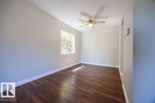 Room featuring wood-finish flooring, a rectangular window, a ceiling fan with integrated lighting, and white baseboards - 8714 164 Street, Edmonton, AB 