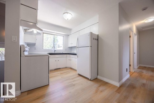 Bright kitchen featuring white cabinetry, black countertops, a stainless steel sink, and light wood-finish flooring - 8714 164 Street, Edmonton, AB 