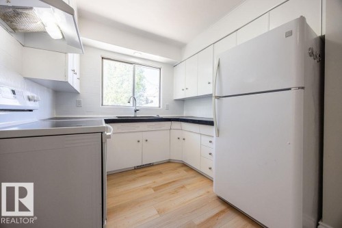 Kitchen featuring a large window, white cabinetry, dark countertops, a white refrigerator, and wood-finish flooring - 8714 164 Street, Edmonton, AB 