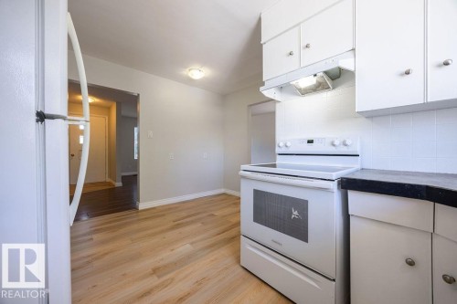 Bright kitchen featuring white cabinetry, dark countertops, a white electric range, and wood-finish flooring - 8714 164 Street, Edmonton, AB 