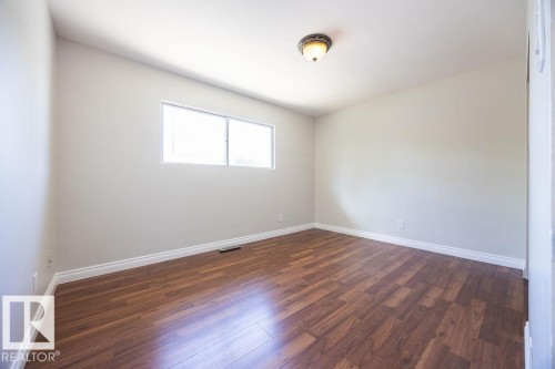 Bright interior room featuring wood-finish flooring, white baseboards, a rectangular window, light gray walls, and a ceiling-mounted light fixture - 8714 164 Street, Edmonton, AB 