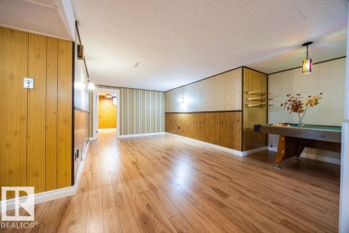 Spacious room featuring wood-finish flooring, wood paneling, and a drop ceiling - 8714 164 Street, Edmonton, AB 