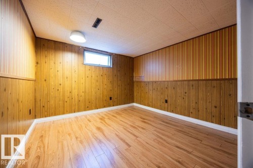 Finished room featuring wood-finish flooring, wood paneling, a drop ceiling, and a single window - 8714 164 Street, Edmonton, AB 