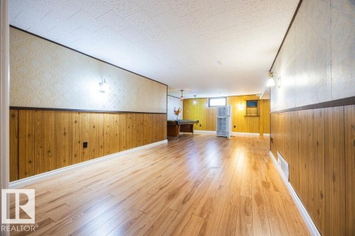 Spacious room with wood-finish flooring, wood paneling, and wall sconces - 8714 164 Street, Edmonton, AB 