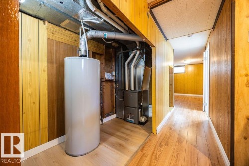 Utility room featuring a water heater, furnace, exposed ductwork, wood-finish flooring, and wood paneling on walls - 8714 164 Street, Edmonton, AB 