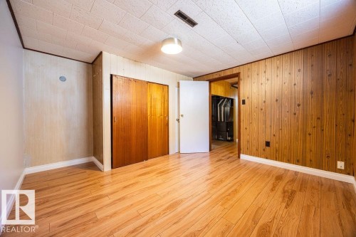 Room featuring wood-finish flooring, a textured ceiling, and wood paneling on multiple walls - 8714 164 Street, Edmonton, AB 