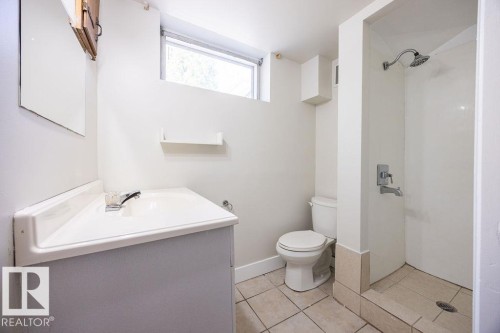 Bathroom featuring a white vanity with integrated sink, chrome faucet, tiled flooring, toilet, and a stand-up shower with a rain showerhead - 8714 164 Street, Edmonton, AB 
