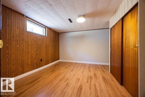 Room featuring wood-finish flooring, a rectangular window, light-toned wall paint, wood paneled wall, and integrated ceiling lighting - 8714 164 Street, Edmonton, AB 