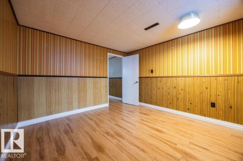 Room featuring wood-finish flooring, wood paneling wainscoting, striped wallpaper, white baseboards, and a dropped ceiling with recessed lighting - 8714 164 Street, Edmonton, AB 