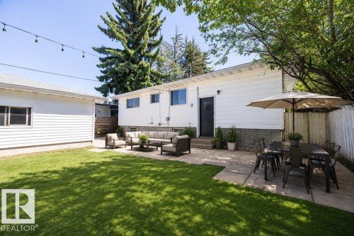 Expansive backyard featuring a manicured lawn, a large paver patio, and a detached garage with horizontal siding. Virtually Staged Photo. - 8714 164 Street, Edmonton, AB 