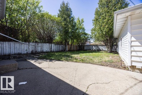 Expansive backyard featuring a concrete patio, a grass lawn, mature trees, and a perimeter fence - 8714 164 Street, Edmonton, AB 