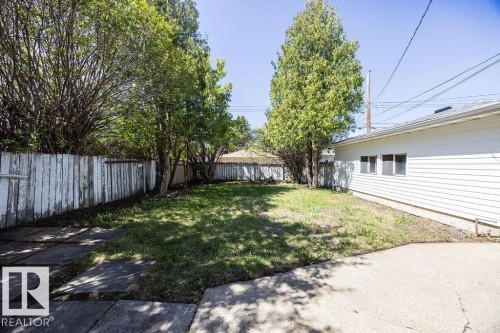 Expansive rear yard featuring a grass lawn, mature perimeter trees, and a wooden fence - 8714 164 Street, Edmonton, AB 