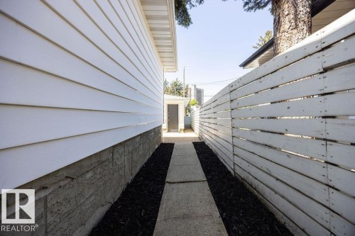 Side yard pathway featuring concrete pavers, dark ground cover, and a white plank fence - 8714 164 Street, Edmonton, AB 