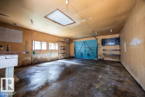 Spacious utility area featuring a garage door, multiple windows, built-in shelving, a workbench, and overhead lighting - 8714 164 Street, Edmonton, AB 