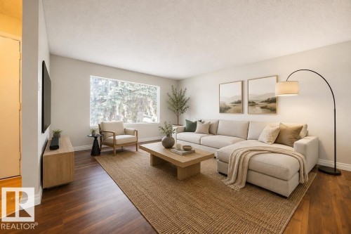 Spacious living area featuring wood-finish flooring, a large picture window, light neutral wall tones, and white baseboards. Photo Virtually Staged. - 8714 164 Street, Edmonton, AB 