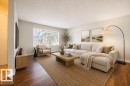 Spacious living area featuring wood-finish flooring, a large picture window, light neutral wall tones, and white baseboards. Photo Virtually Staged. - 8714 164 Street, Edmonton, AB 