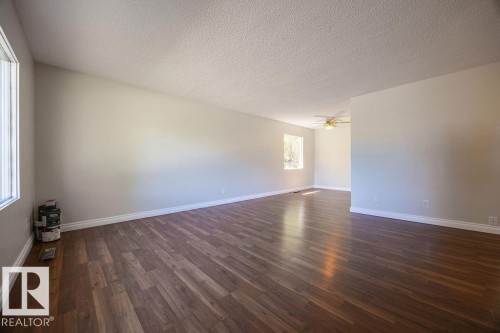Spacious room featuring wood-finish flooring, light-toned walls, multiple windows, and a ceiling fan in the far portion of the space - 8714 164 Street, Edmonton, AB 