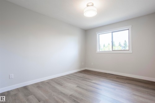 Light grey wall paint and wood-finish flooring in a bright room featuring a window with white trim - 738 Kananaskis Drive, Devon, AB - Indoor Photo Showing Other Room
