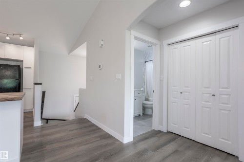 Entryway with wood-finish flooring, white bi-fold closet doors, recessed lighting, and an archway leading to a bathroom featuring a white vanity and toilet - 738 Kananaskis Drive, Devon, AB - Indoor