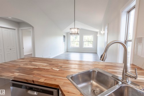 Kitchen island featuring butcher block countertops and a stainless steel double basin sink with a pull-down faucet - 738 Kananaskis Drive, Devon, AB - Indoor Photo Showing Kitchen With Double Sink