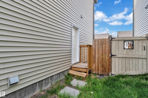 Side exterior featuring light-colored horizontal siding, a wooden gate with decorative window detail, a small wooden deck with stairs, and concrete stepping stones - 432 Watt Boulevard, Edmonton, AB - Outdoor