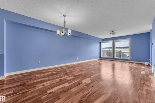 Spacious room featuring wood-finish flooring, two large windows, a ceiling-mounted light fixture, and a contemporary chandelier - 432 Watt Boulevard, Edmonton, AB - Indoor Photo Showing Other Room