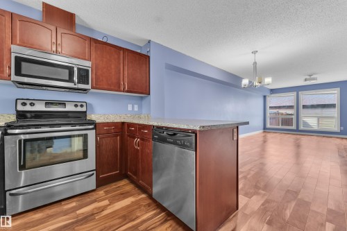 Kitchen featuring stainless steel appliances, dark wood cabinetry, and a peninsula with a stone-finish countertop - 432 Watt Boulevard, Edmonton, AB - Indoor Photo Showing Kitchen With Stainless Steel Kitchen