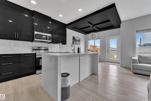 Contemporary kitchen featuring high-gloss black cabinetry, stainless steel appliances, and a white countertop island with an integrated sink - 1118 Goldfinch Crescent, Edmonton, AB - Indoor Photo Showing Kitchen