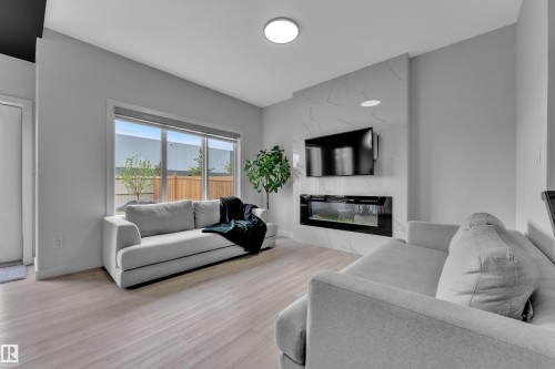 Living area featuring light wood-finish flooring, a large window, and a built-in electric fireplace with a white marble-effect surround - 1118 Goldfinch Crescent, Edmonton, AB - Indoor Photo Showing Living Room With Fireplace