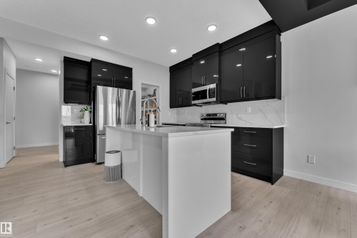 Modern kitchen featuring a white island, black cabinetry, stainless steel appliances, light wood-finish flooring, and recessed lighting - 1118 Goldfinch Crescent, Edmonton, AB - Indoor Photo Showing Kitchen With Upgraded Kitchen