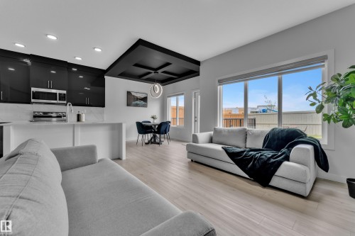 Open-concept living space with light wood-finish flooring, featuring a kitchen with black cabinetry, a white countertop island, and stainless steel appliances - 1118 Goldfinch Crescent, Edmonton, AB - Indoor Photo Showing Living Room