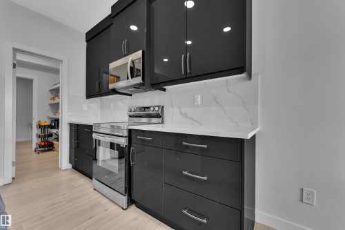 Contemporary kitchen featuring high-gloss black cabinetry, stainless steel appliances, white countertops, and a full-height white veined backsplash - 1118 Goldfinch Crescent, Edmonton, AB - Indoor Photo Showing Kitchen