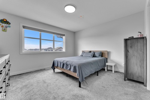 Bright bedroom featuring a large window with white trim, light gray carpeting, and a flush-mount ceiling light - 1118 Goldfinch Crescent, Edmonton, AB - Indoor Photo Showing Bedroom