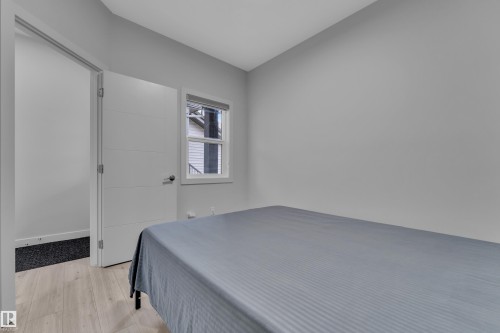 Bedroom featuring light wood-finish flooring, a contemporary white door with horizontal paneling, and a single window with blinds - 1118 Goldfinch Crescent, Edmonton, AB - Indoor