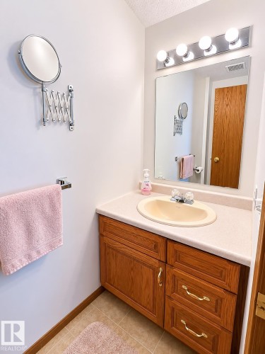 Bathroom vanity featuring a light-toned countertop with an integrated sink, wood-finish cabinetry, and a chrome light fixture - 4005 55 Avenue, Whitecourt, AB - Indoor Photo Showing Bathroom