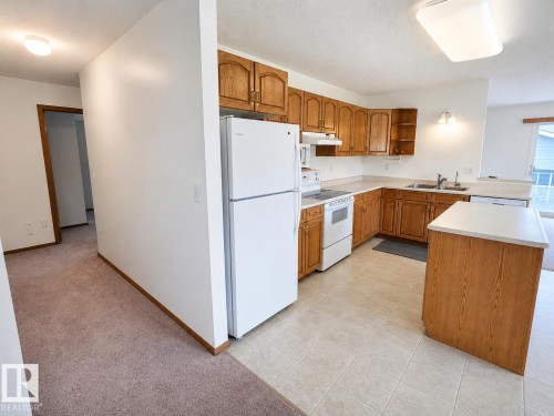 U-shaped kitchen featuring wood cabinetry, white appliances, laminate countertops, and tile flooring - 4005 55 Avenue, Whitecourt, AB - Indoor Photo Showing Kitchen With Double Sink