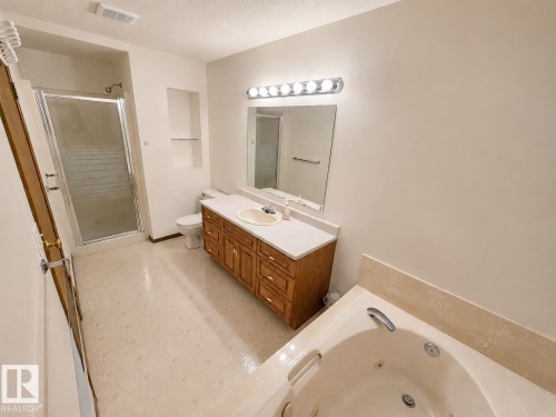 Spacious bathroom featuring a built-in jetted tub, a separate glass-enclosed shower, a single vanity with wood-finish cabinetry, a built-in mirror, and recessed wall shelving - 4005 55 Avenue, Whitecourt, AB - Indoor Photo Showing Bathroom