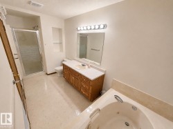 Spacious bathroom featuring a built-in jetted tub, a separate glass-enclosed shower, a single vanity with wood-finish cabinetry, a built-in mirror, and recessed wall shelving - 