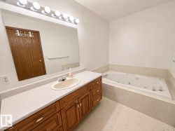 Bathroom featuring a built-in jetted tub, wood-finish vanity with an integrated sink, and a large wall-mounted mirror - 