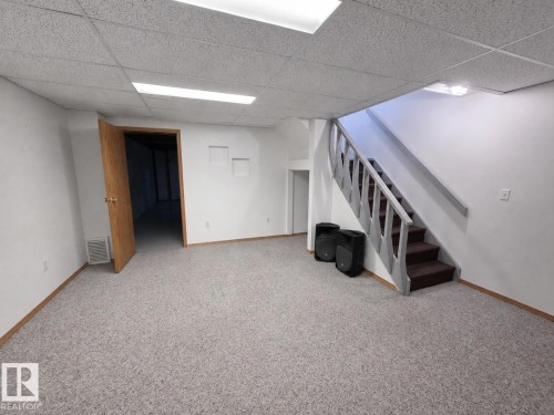 Finished basement space featuring light gray textured carpeting, white painted walls, and a drop ceiling with integrated lighting - 4005 55 Avenue, Whitecourt, AB - Indoor