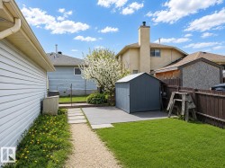 Expansive backyard featuring a manicured lawn, a gravel pathway, concrete stepping stones, a composite deck, and a gray storage shed - 