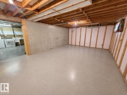 Unfinished basement featuring exposed wood joists, concrete flooring, and framed perimeter walls with insulation - 