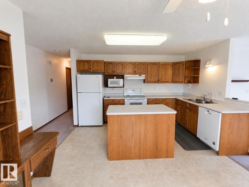 Open-concept kitchen featuring wood-finish cabinetry, a central island, and white appliances - 4005 55 Avenue, Whitecourt, AB - Indoor Photo Showing Kitchen With Double Sink