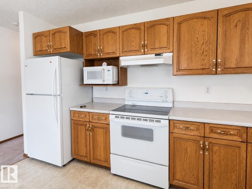 Kitchen featuring wood cabinetry, white appliances, light-toned countertops, tile flooring, and a built-in microwave shelf - 4005 55 Avenue, Whitecourt, AB - Indoor Photo Showing Kitchen