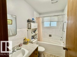Bathroom featuring a bathtub with subway tile surround, white vanity, integrated sink, and a window with horizontal blinds - 