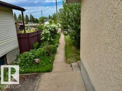 Concrete walkway bordered by mature greenery and a dark wood fence - 