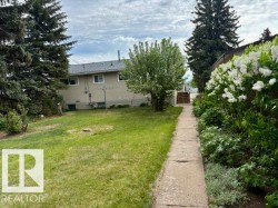 Expansive backyard featuring a concrete pathway, mature trees, and blooming white shrubbery - 