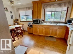 Kitchen featuring wood-finish flooring, wood cabinetry, L-shaped countertop, double basin sink, and a ceiling fan - 