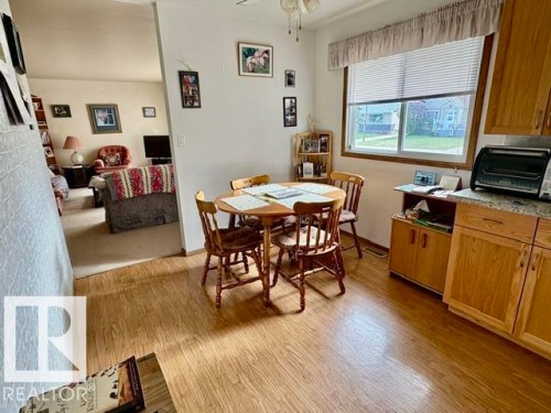 Bright eat-in kitchen area featuring wood-finish flooring, a large window with blinds, and built-in wood cabinetry with a light-colored countertop - 5454 46 Street, Vegreville, AB - Indoor Photo Showing Dining Room